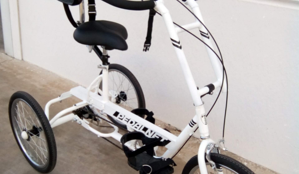 Niña con necesidades especiales sonríe mientras monta una bicicleta adaptada de PedalnetMobility